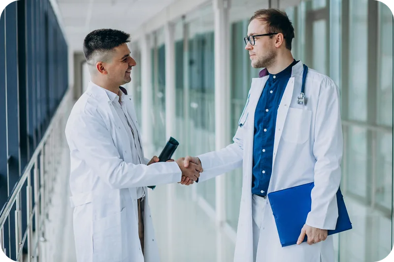 Two physicians shaking hands in a hospital corridor